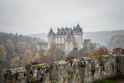 Château fort médiéval français dominant une vallée brumeuse entourée de forêts aux couleurs d'automne